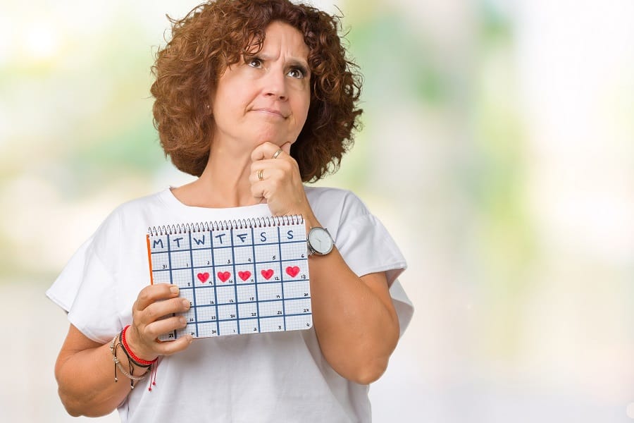 Middle ager senior woman holding menstruation calendar over isolated background serious face thinking about question, very confused idea